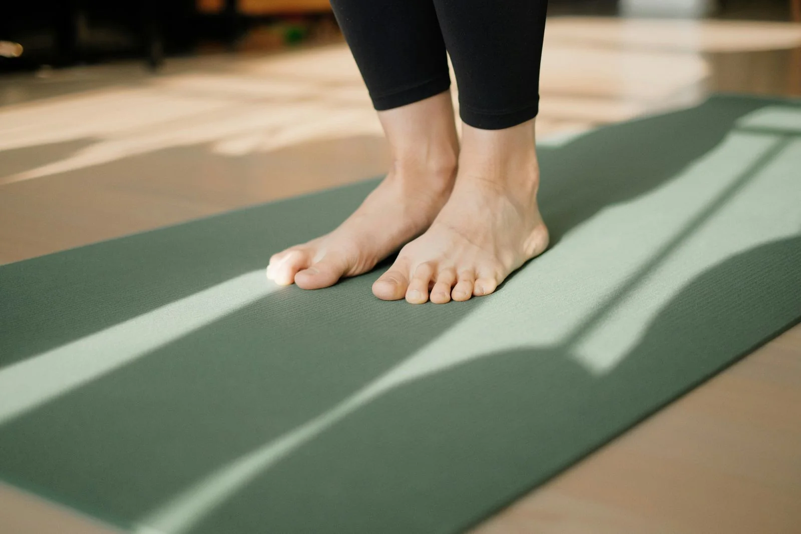 Voeten op een groene yogamat in het zonlicht.